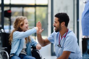 Young doctor having fun with little girl on a wheelchair.